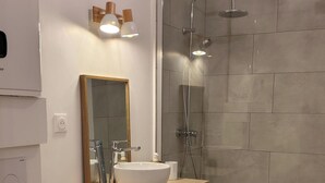 Et moderne badeværelse med toilet, håndvask, spejl og brusebad.