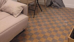 Et lille rum med en sofa, et spisebord med stole, et billede i ramme på væggen og et vindue med gardiner.