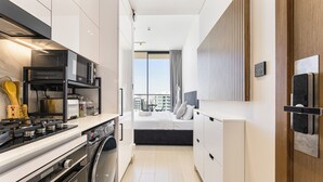 Een moderne keuken met een inbouwmagnetron, fornuis en oven, een wasruimte en een slaapkamer met een groot raam.