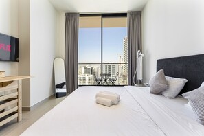 A modern hotel room with a large bed, a desk, a chair, and a TV mounted on the wall. - Modern Studio in JVC Near Dubai Miracle Garden (دبي)