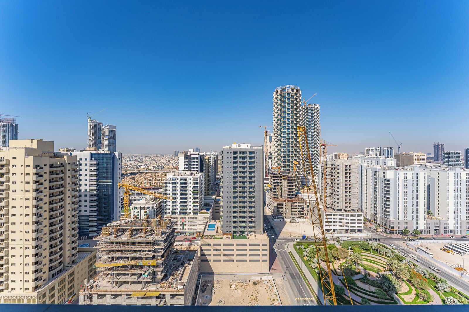 Un paisaje urbano con rascacielos, grúas de construcción y un cielo azul despejado.