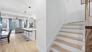 Une cuisine moderne dotée d’un îlot central, d’un coin repas avec une table et des chaises, et d’un escalier avec des marches en bois.