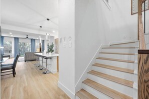 A modern kitchen with a central island, a dining area with a table and chairs, and a staircase with wooden steps. - Upscale 3BR 3.5BA | Patio & Garage | UTSW (Dallas)