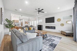 Ein modernes Wohnzimmer mit grauem Sofa, Couchtisch, Kamin, Wand-Fernseher und Deckenventilator.