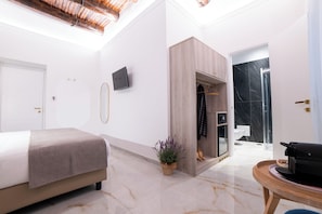 Ein modernes Hotelzimmer mit Bett, einer kleinen Sitzecke, einer Dusche und einem an der Wand befestigten Fernseher.