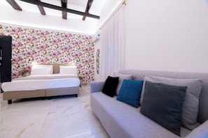 Un dormitorio con cama, sofá, pared floral y techo con vigas de madera.