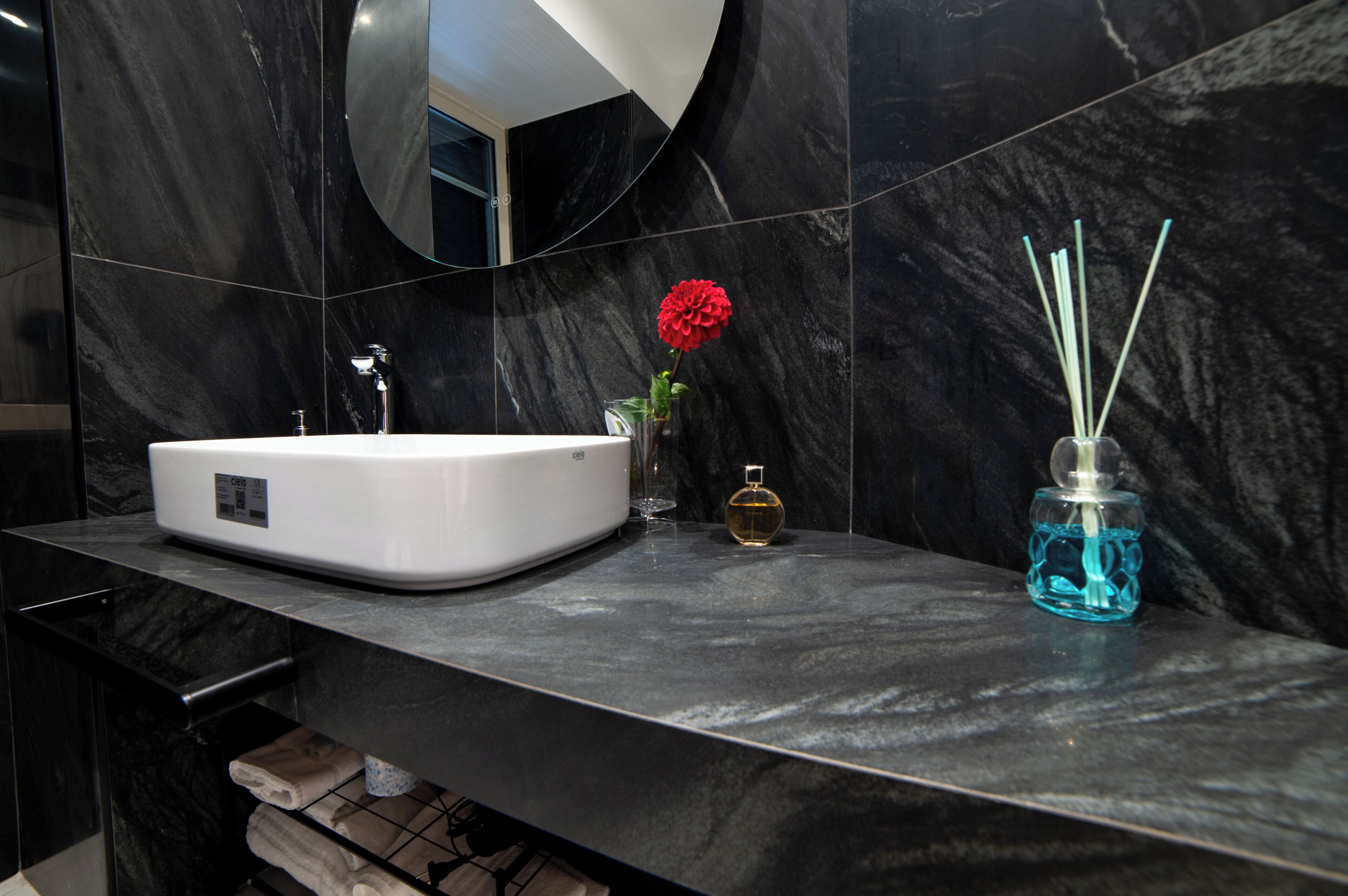 A modern bathroom with a white sink, a mirror, and a vase with a red flower.