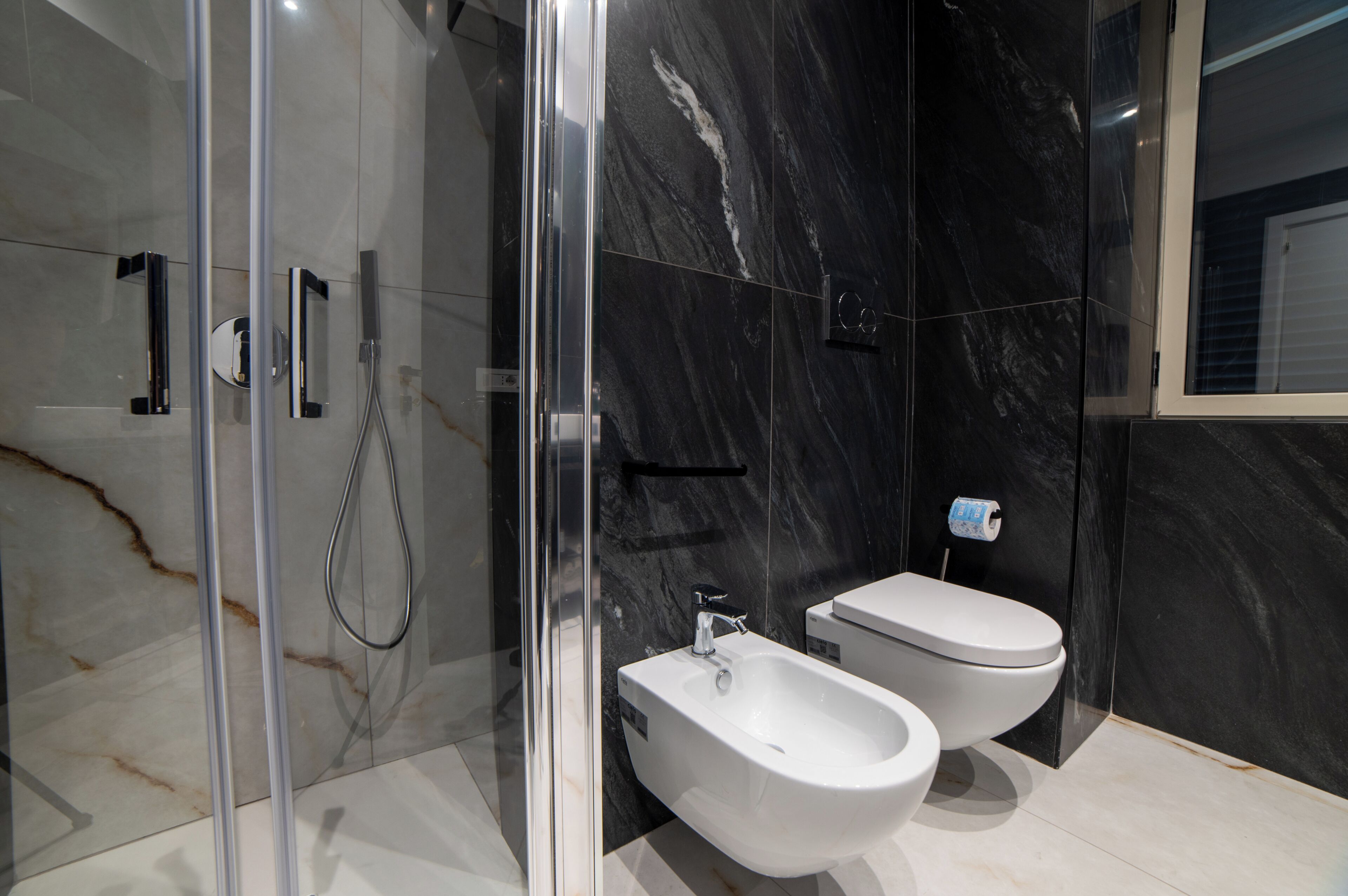 A modern bathroom with a glass shower enclosure, a bidet, and a toilet.