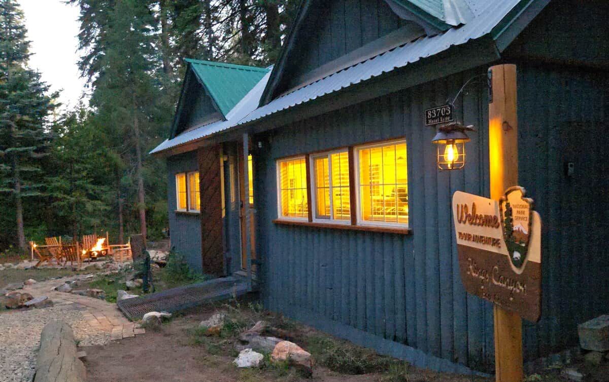 A rustic cabin with a wooden sign, a metal roof, and a lantern.