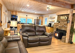 A cozy living room with a fireplace, leather recliner, wooden ceiling, and a stone wall.