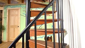 Una escalera de caracol con escalones de madera y barandillas negras, que conduce a una habitación con una pared verde y un mapa.