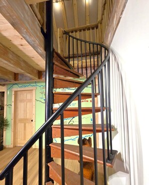 Una escalera de caracol con escalones de madera y barandillas negras, que conduce a una habitación con una pared verde y un mapa.