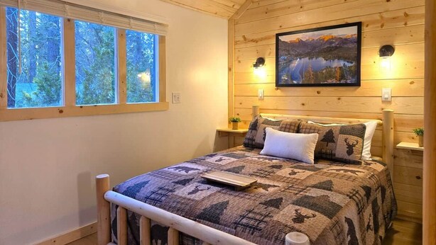 Un dormitorio con paneles de madera, una cama, un cuadro y una ventana con vistas a árboles.