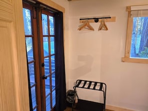 A room with a wooden door, a black metal rack, and a window with a view of trees.