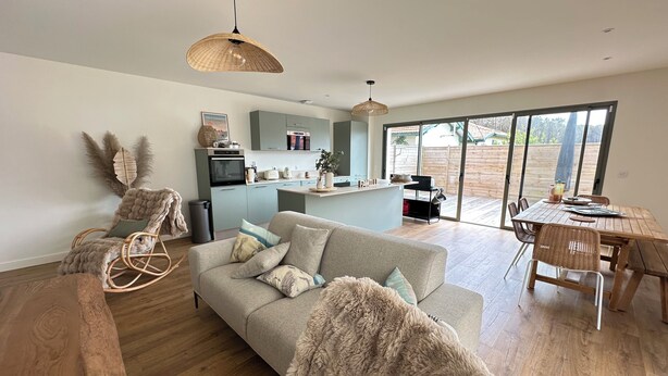 A modern living room with a sofa, a dining table, and a kitchen area with a view through large glass doors. - Comfortable villa 2 minutes from the beach with large terrace, 4 bedrooms (Biscarrosse)