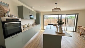 A modern kitchen with a built-in oven, a coffee maker, and a dining area with a table and chairs. - Comfortable villa 2 minutes from the beach with large terrace, 4 bedrooms (Biscarrosse)