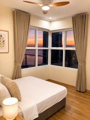 A bedroom with a bed, a ceiling fan, a nightstand, and a window with curtains. - 2BR Malate Bayview Mansion, high floor seaview 26B (Manila)