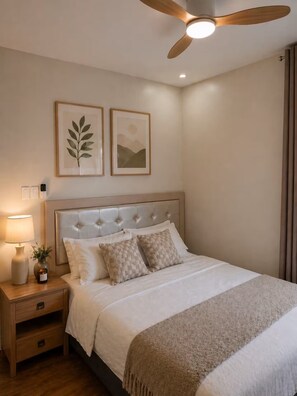 Ein Schlafzimmer mit einer gepolsterten Kopfteile, einem Bett mit weißer Bettwäsche und zwei Kissen, einem Nachttisch mit Lampe und Vase sowie zwei gerahmten Bildern an der Wand.