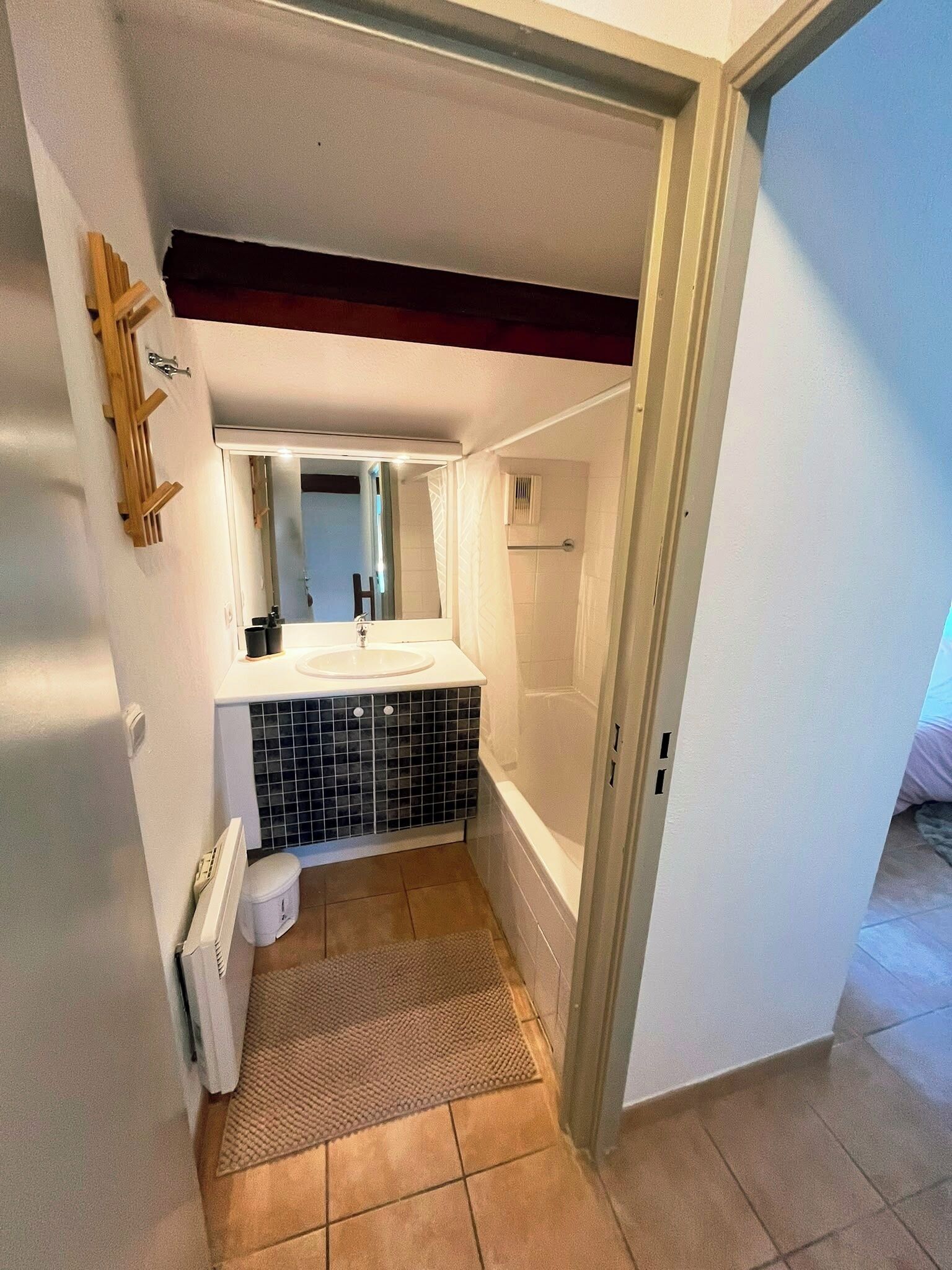 Un baño pequeño con un lavamanos blanco, salpicadero de azulejos negros, ducha y un espejo pequeño.