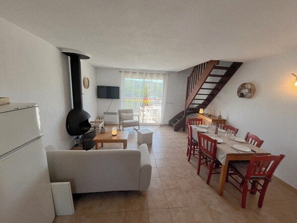 A compact living space with a kitchenette, a sofa, a dining table with chairs, a TV, and a staircase.