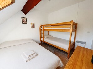 A bunk bed with a lower bunk, a single bed, and a wooden table in a room with white walls and a sloped ceiling.