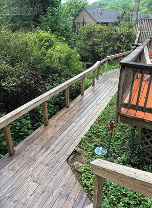 Une terrasse en bois avec une rambarde, entourée d’une végétation luxuriante et avec une maison en arrière-plan.