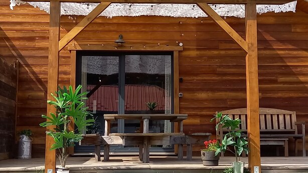 Eine Holzhütte mit überdachter Veranda, Blumentöpfen und blauem Himmel.