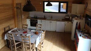 Eine kleine Küche mit Holzwänden, einem Esstisch mit Stühlen, einem Fenster und einem Kühlschrank.