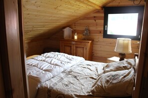 Une chambre avec un plafond en bois, un lit avec une literie blanche, une table de chevet avec une lampe et une fenêtre avec des stores.