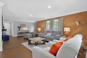 Ein modernes Wohnzimmer mit einem grauen Sofa, weißen Sesseln, einem Couchtisch und einer Lampe.