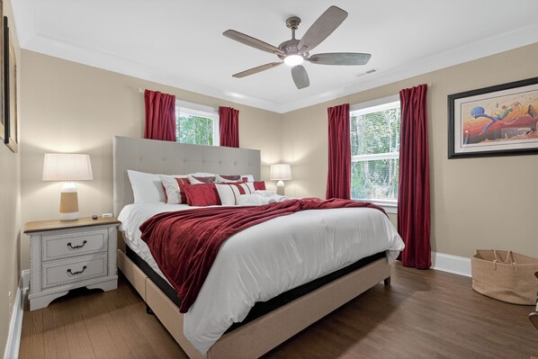 Ein Schlafzimmer mit Bett, Nachttischen, Deckenventilator und einem Fenster mit Vorhängen.