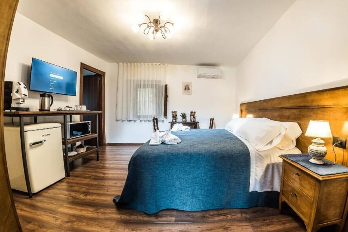 A hotel room with a bed, bedside table, TV, desk, and a small kitchenette.