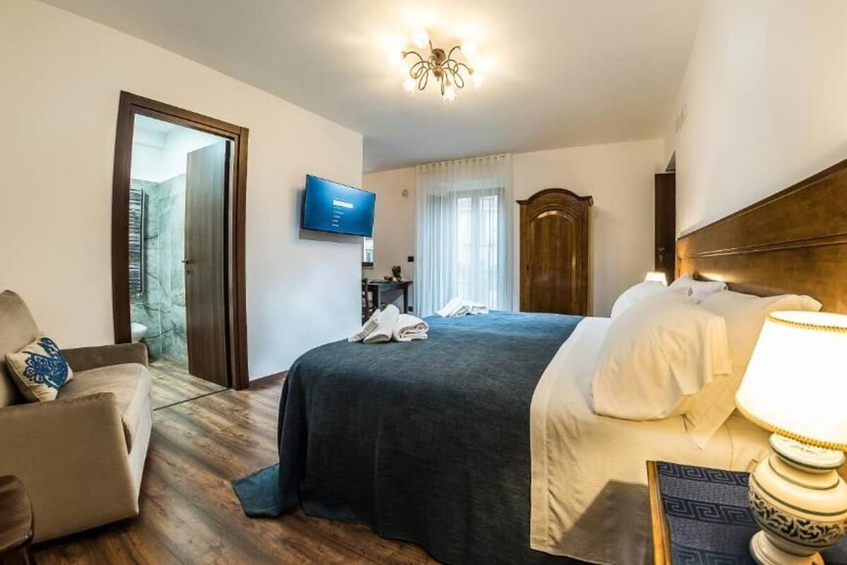 A hotel room with a bed, a desk, a chair, a television, and a wooden headboard.
