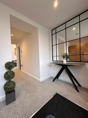 A modern hallway with a black-framed mirror, a potted plant, and a carpeted floor.