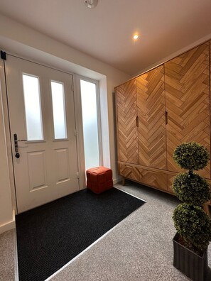 A modern interior with a white door, a herringbone-patterned wardrobe, a black doormat, and a small orange ottoman. - Stylish 2-Bed Getaway | Work & Recharge (Worksop)