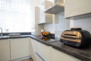 A modern kitchen with white cabinetry, a stainless steel range hood, a built-in oven, and a fruit bowl on the countertop. - Stylish 2-Bed Getaway | Work & Recharge (Worksop)