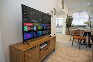 A flat-screen TV on a wooden stand with a remote control, displaying a streaming service interface. - Stylish 2-Bed Getaway | Work & Recharge (Worksop)