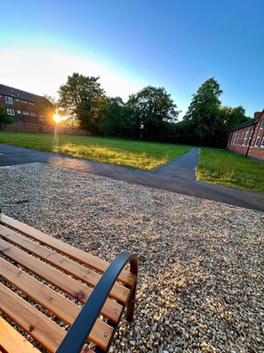 A bench with a gravel path, a grassy area, and a building in the background. - Stylish 2-Bed Getaway | Work & Recharge (Worksop)