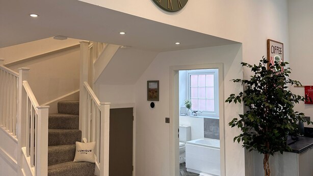 Una escalera con un cojín 'LUMIQUE Living', un reloj de pared, una planta en maceta y un cartel que dice 'COFFEE'.
