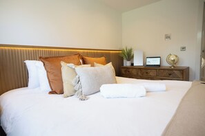 A neatly made bed with multiple pillows and a white blanket, a wooden headboard with a lighted panel, a wooden nightstand with a laptop, a globe, and a plant. - Stylish 2-Bed Getaway | Work & Recharge (Worksop)