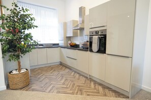 Una cocina moderna con armarios blancos, piso de madera en patrón de espiga y horno empotrado, además de una planta en maceta.