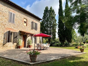 Un bâtiment en pierre doté d’une terrasse, de mobilier d’extérieur et d’un parasol rouge.