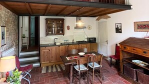 A rustic kitchen with wooden cabinets, a dining table with chairs, and a balcony with red cushions.
