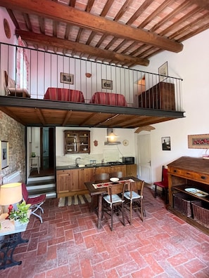 Une cuisine rustique avec des meubles en bois, une table à manger avec des chaises et un balcon agrémenté de coussins rouges.