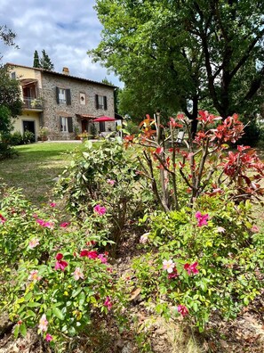 A stone building with a balcony, surrounded by a garden with flowering plants. - Tuscan country house (Larciano)