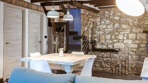 A dining area with a wooden table and chairs, a stone wall, and a staircase.