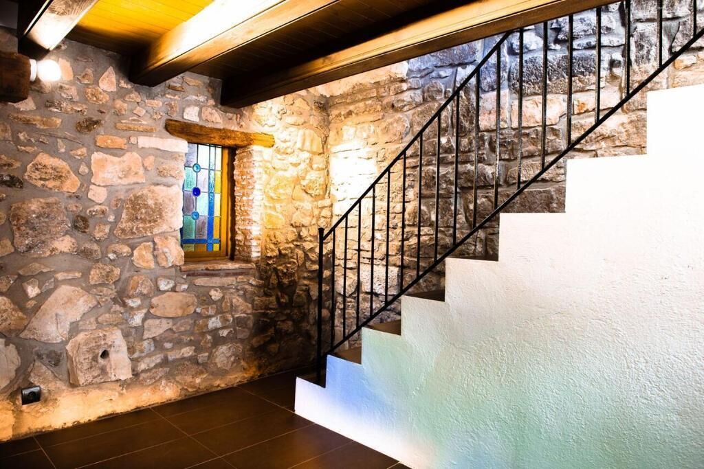 Uma parede de pedra, uma escadaria com grades pretas e uma janela com vitrais.