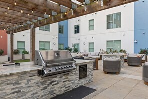 Eine Terrasse im Freien mit integriertem Grill, Sitzgelegenheit und einer Pergola mit Lichterketten.