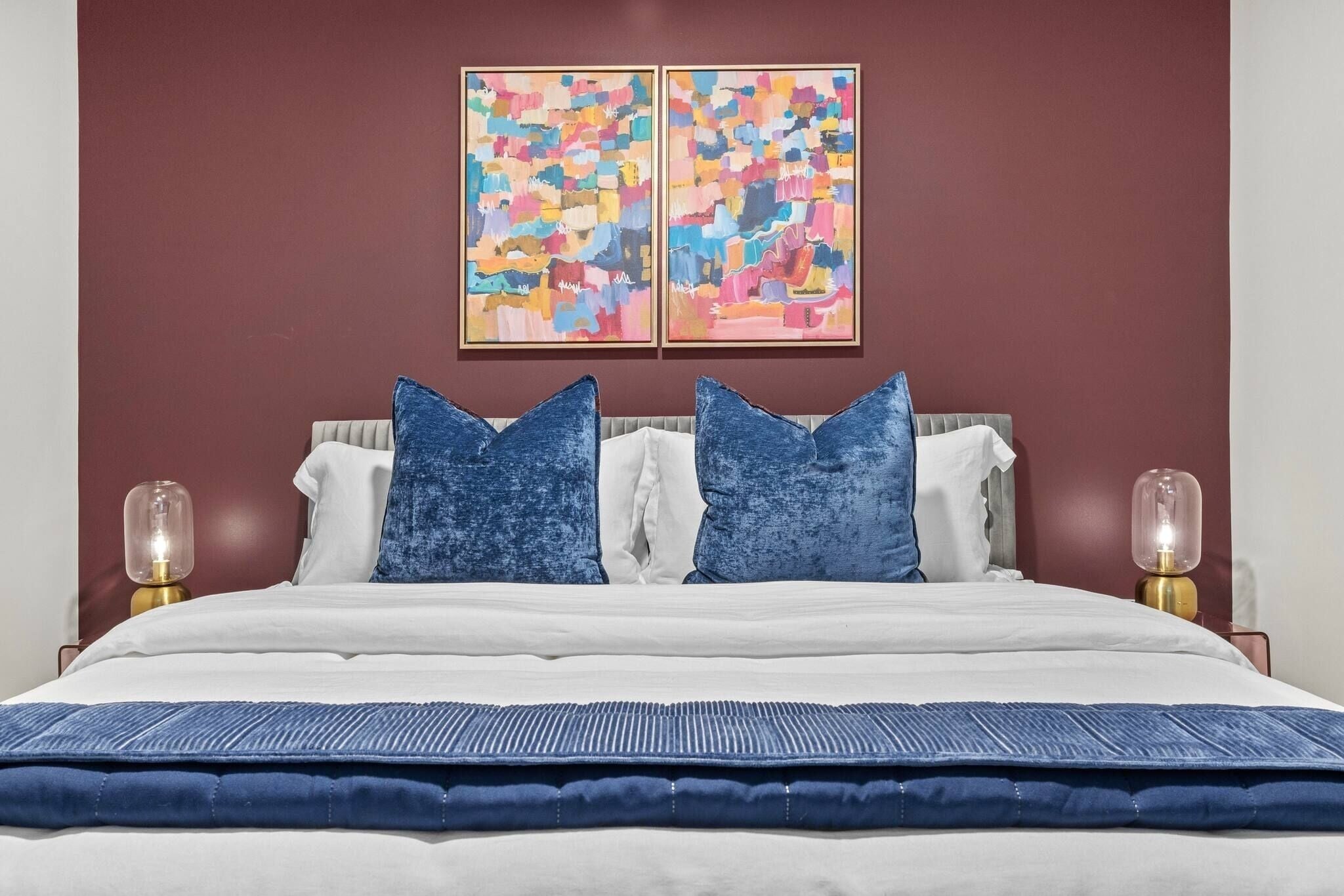 A bed with a white and blue bedspread, two blue pillows, and two wall-mounted lamps.