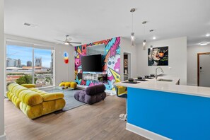 Ein modernes Wohnzimmer mit großem Fernseher, farbenfrohen Kunstwerken und Blick auf die Stadt.